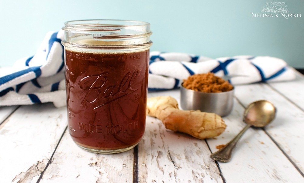 A glass of ginger water with ginger, brown sugar and a spoon on a counter.