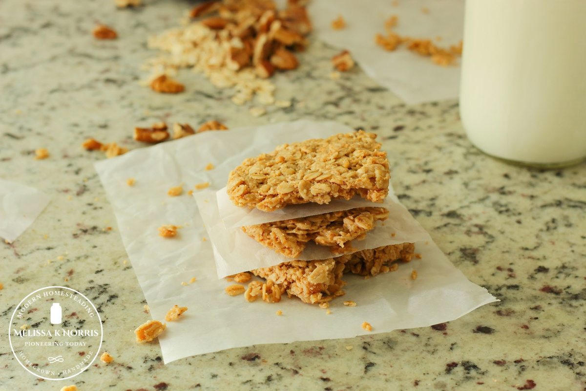 Homemade granola bars stacked up with parchment paper in between layers and granola on the counter behind them.