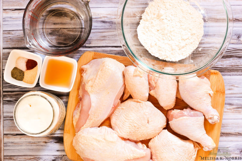 Chicken parts on a cutting board with dredging ingredients.