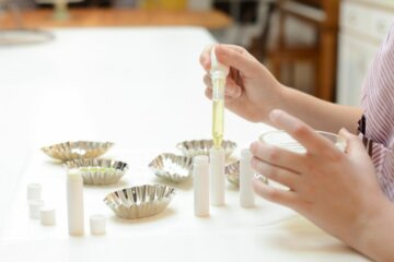 A photo of someone making homemade lip balm, using a dropper adding the liquid into tubes.