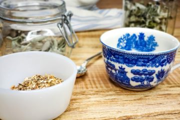 Blue and white tea cup next to dried herbs in jars.