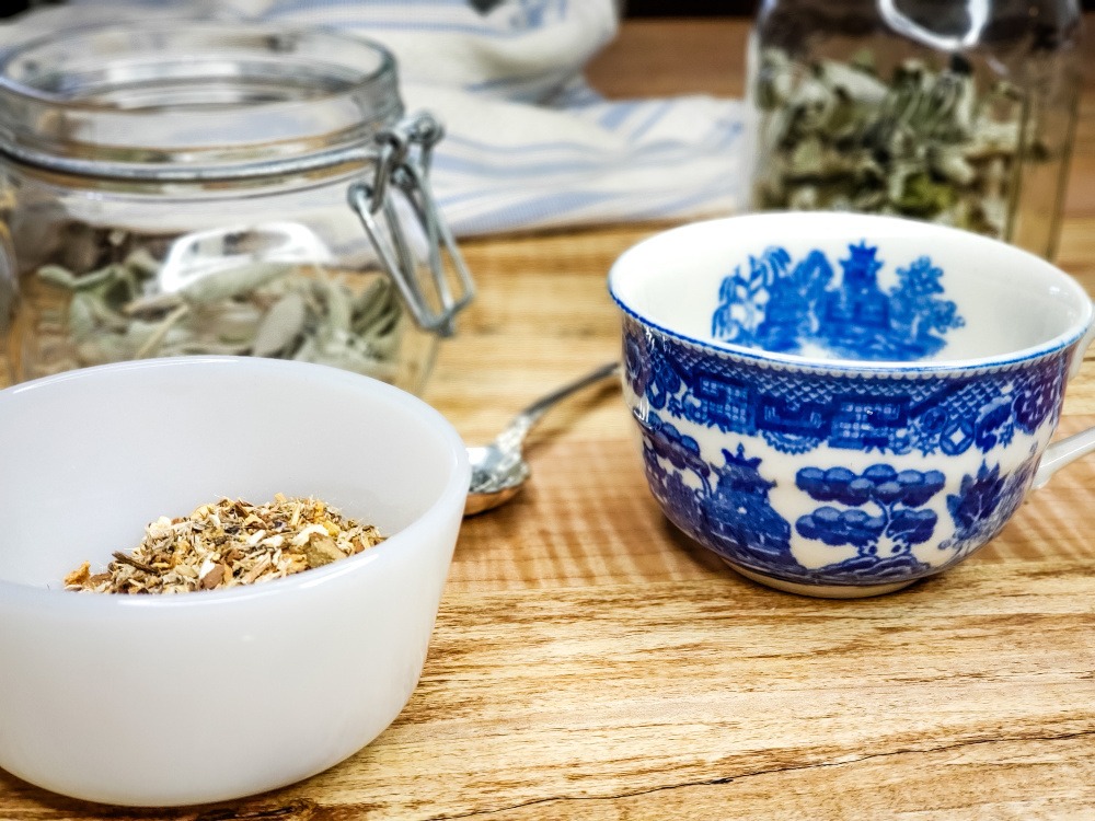 Blue and white tea cup next to dried herbs in jars.