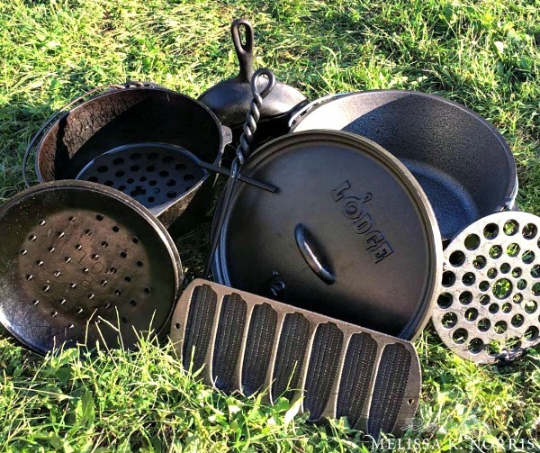 A bunch of cast iron cookware stacked in the grass.