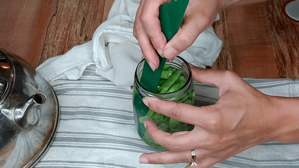 A woman removing air bubbles from a jar of green beans before canning.