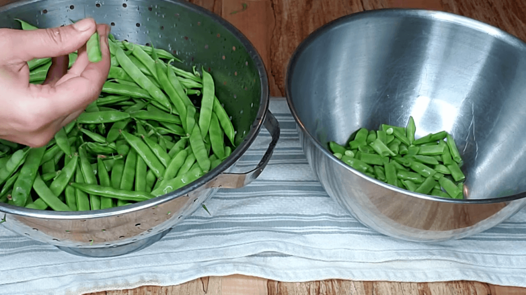 Green beans in a bowl being snapped.