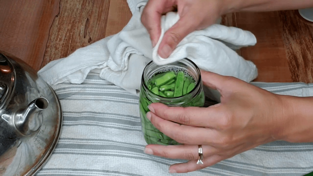 Jars of green beans with a woman wiping the rim clean.