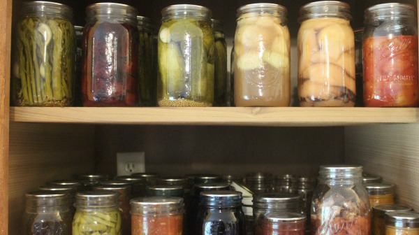 Canning jars filled with various foods on a pantry shelf.