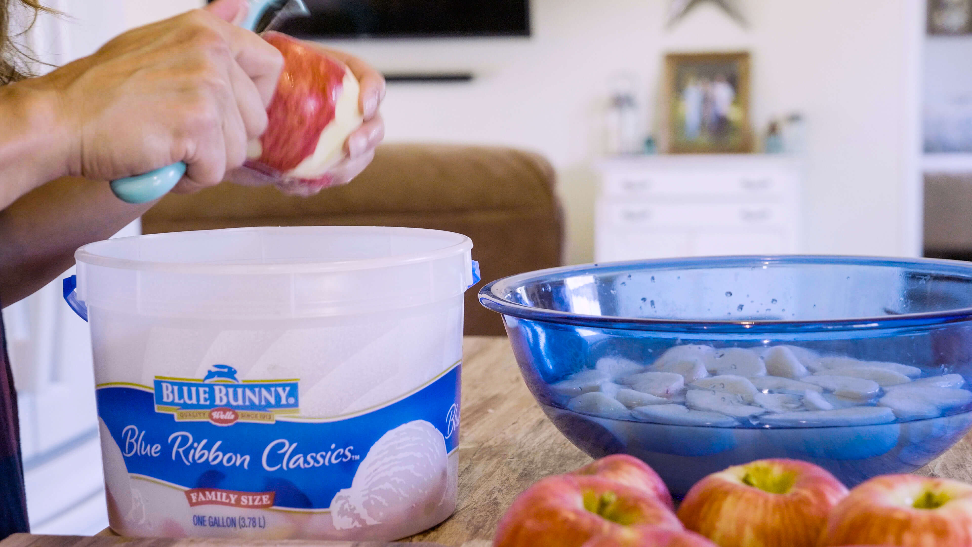 Hands peeling an apple with a bowl filled with chopped apples next to it.