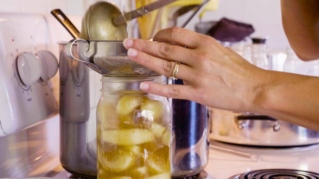 A woman ladling apple pie filling into a mason jar.