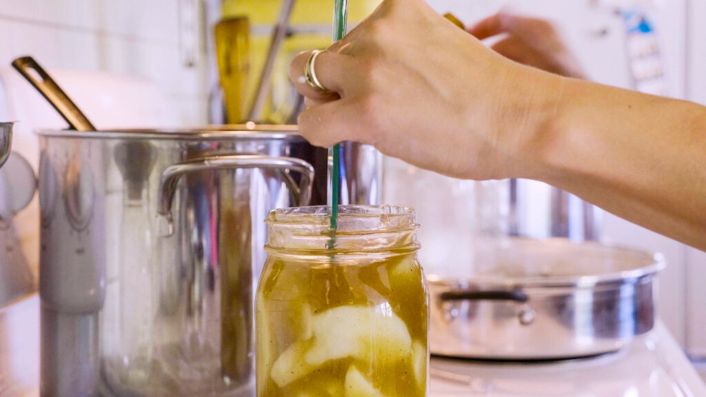 A woman's hand measuring the head space in a mason jar filled with apple pie filling.