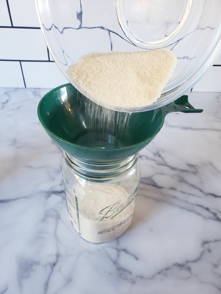 Sugar being poured through a funnel into a mason jar.