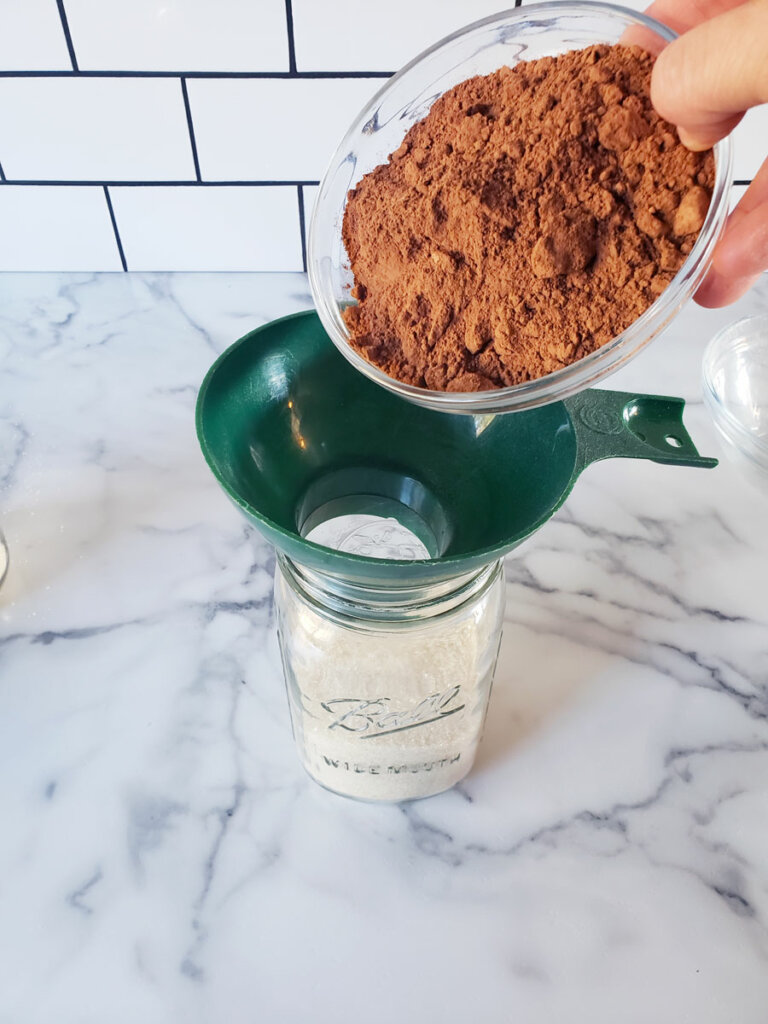 Cocoa powder being poured through a funnel into a mason jar.