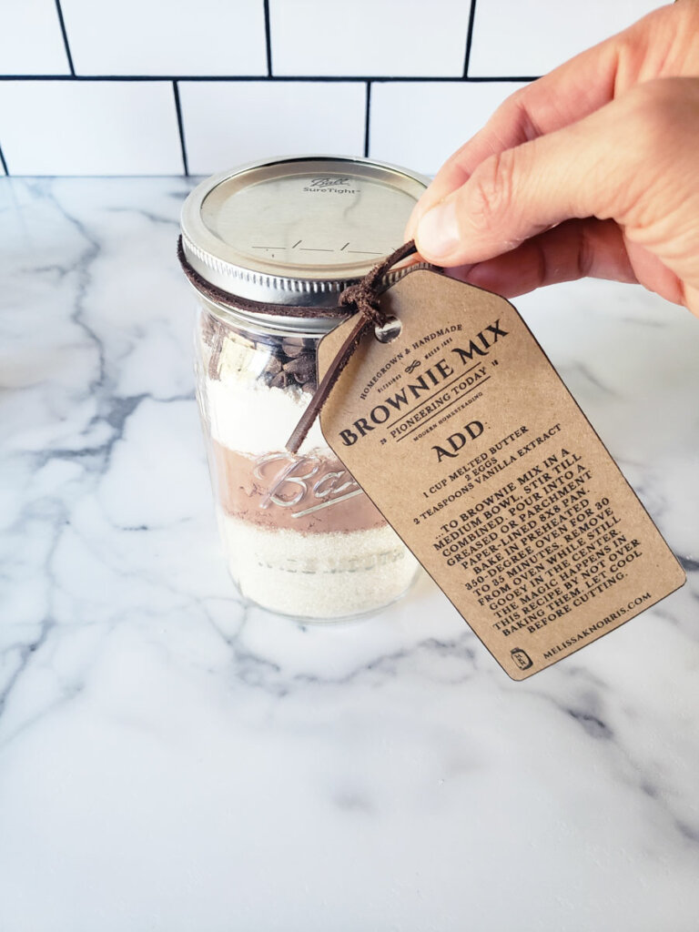 A tag being added to a mason jar filled with brownie mix ingredients.