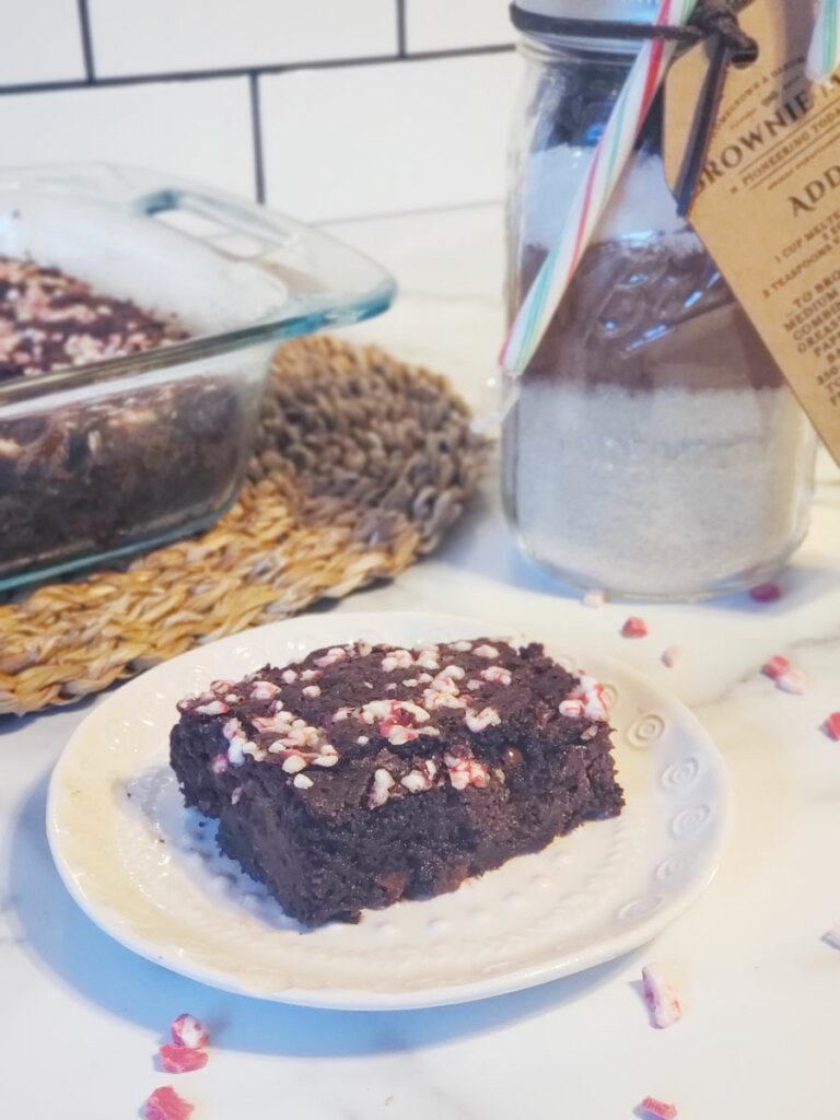 A brownie on a plate with a pan of brownies and a jar of brownie mix in the background.