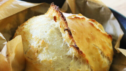 Finished loaf of artisan bread in a cast iron dutch oven lined with parchment paper.