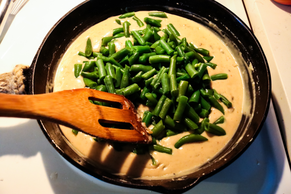 Green beans being added to a pan of homemade cream of mushroom soup.