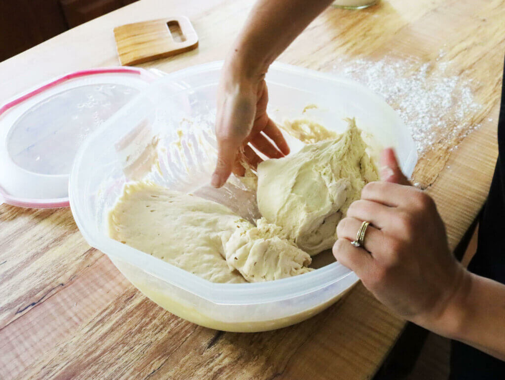 A woman's hand scooping out half the dough from a large bowl.