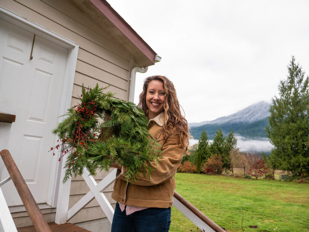 A woman standing outside holding up a Christmas wreath.