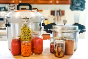 Two pressure canners and jars of home canned food sitting on a kitchen counter.