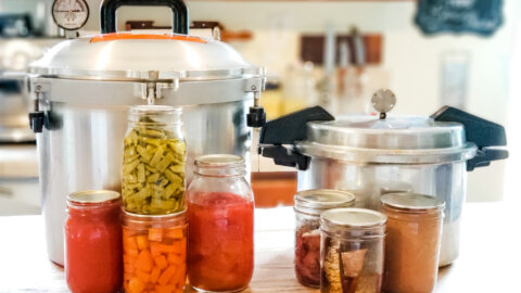 Two pressure canners and jars of home canned food sitting on a kitchen counter.