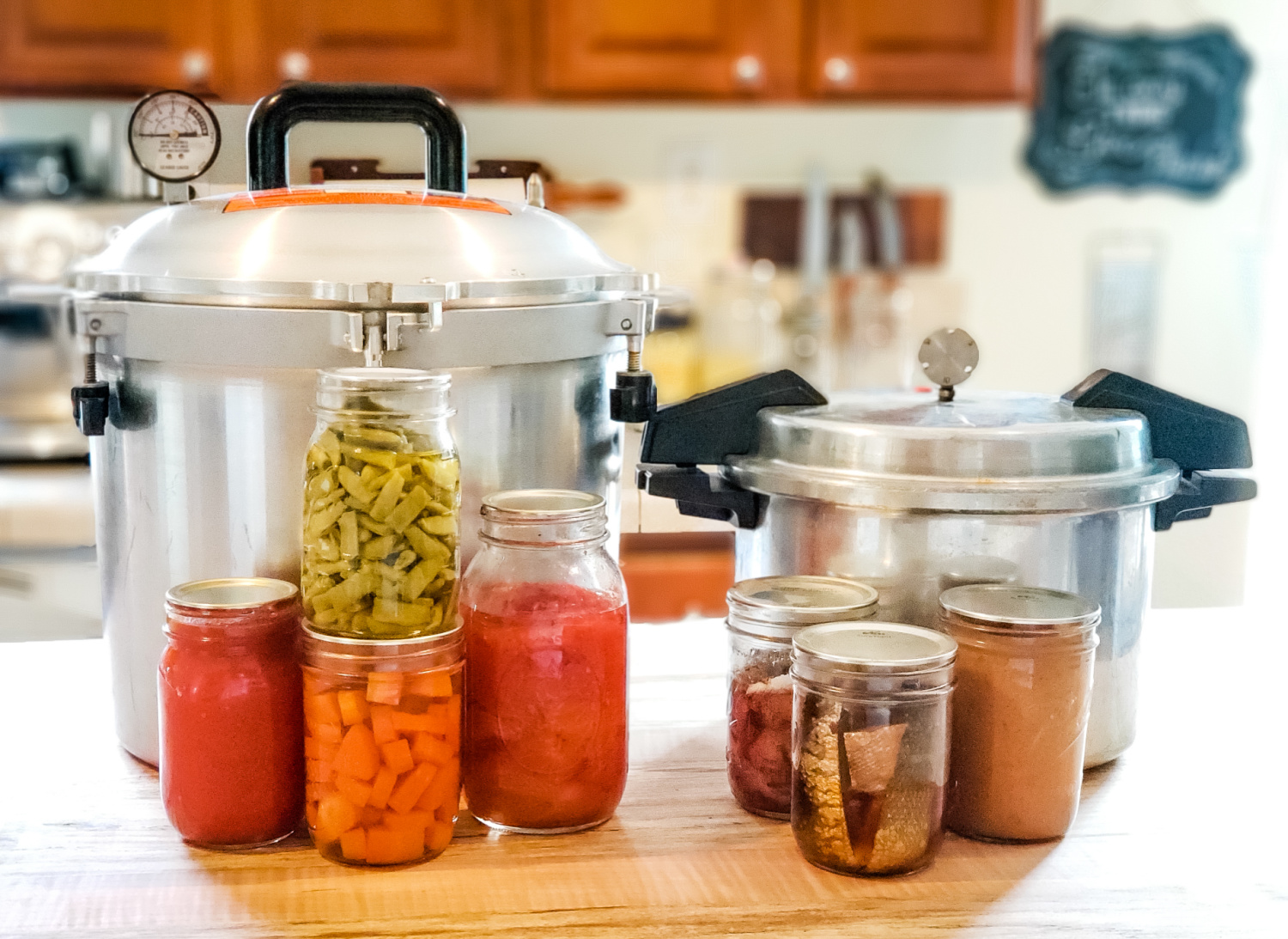 Two pressure canners and jars of home canned food sitting on a kitchen counter.