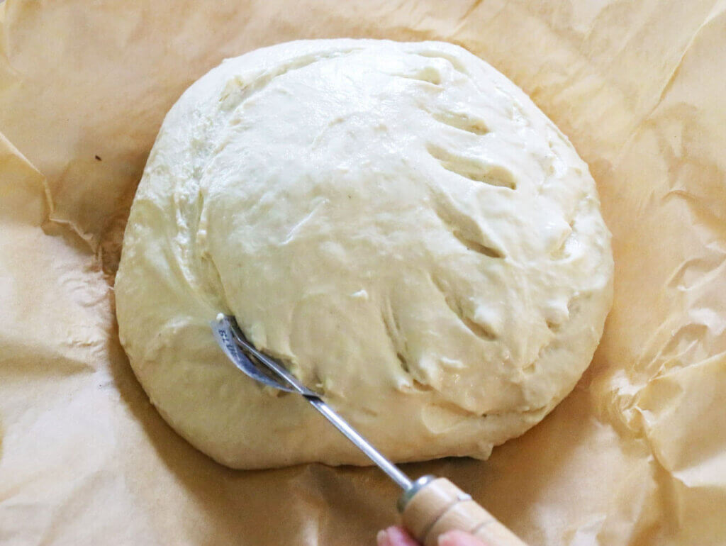 A bread lame scoring a shaped ball of artisan bread dough.