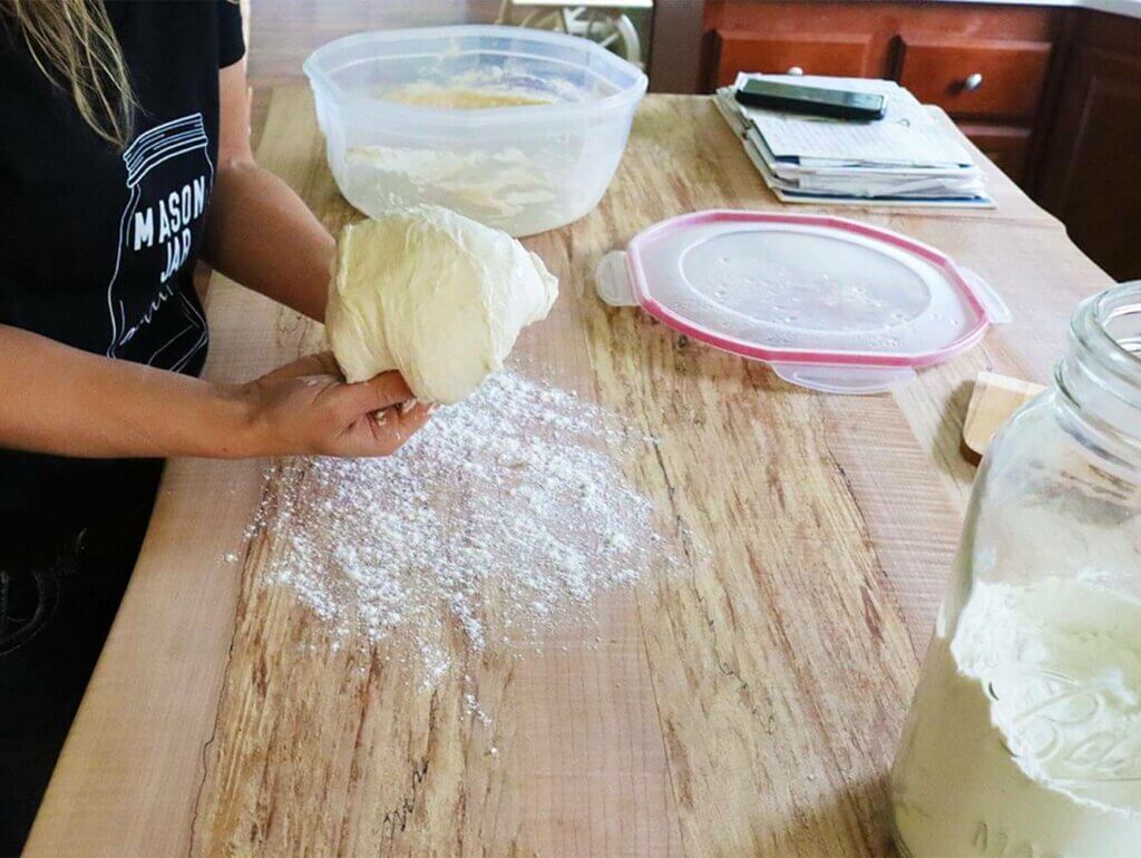 A woman shaping dough with her hands on a well-floured work surface.