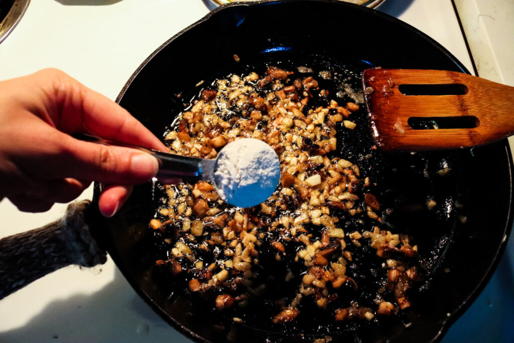 Sprinkling flour into a cast iron pan with butter, onions and chopped mushrooms.