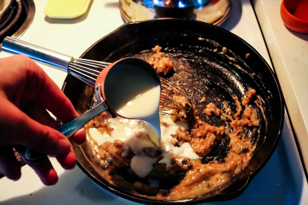 A measuring cup pouring milk into a pan to make homemade cream of mushroom soup.