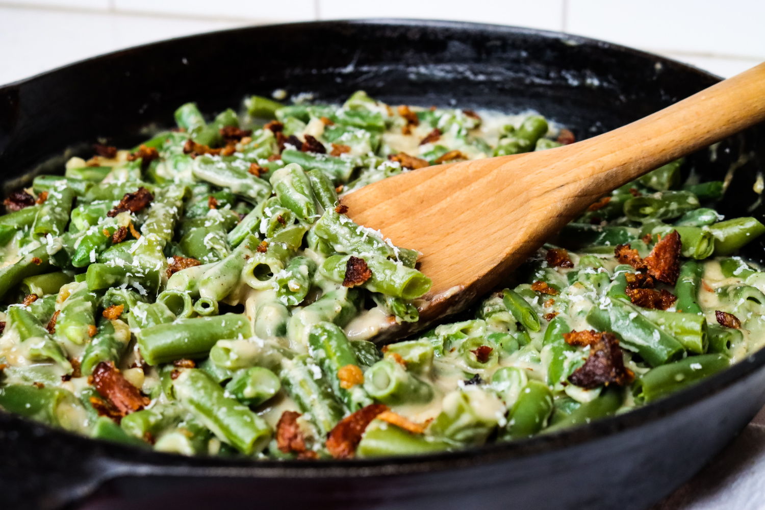 Cast iron skillet with green bean casserole and a wooden spoon.