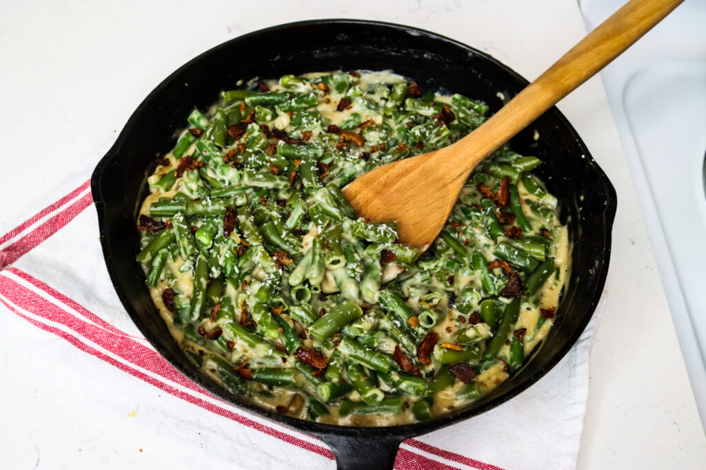 Cast iron pan with green bean casserole and a wooden spoon.