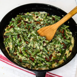 Cast iron pan with green bean casserole and a wooden spoon.