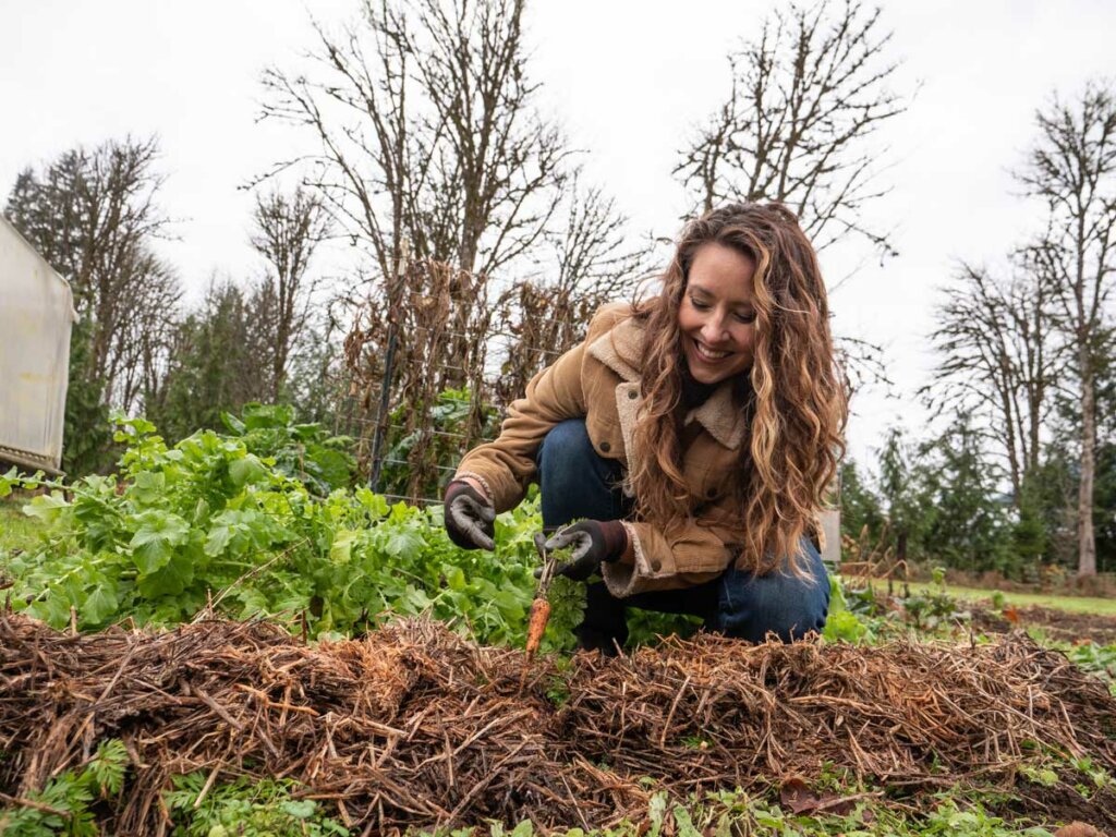 A woman in the garden holding up a carrot just pulled from the ground.