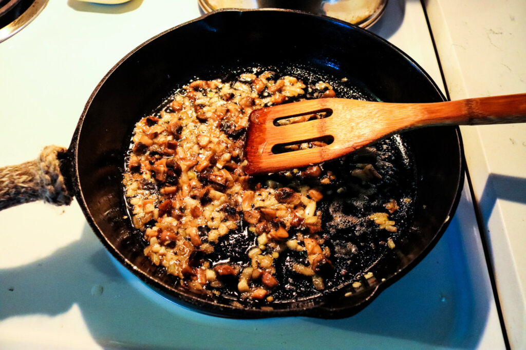 A wooden spatula stirring onions and mushrooms in a cast iron pan.