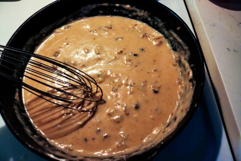 A whisk stirring a cast iron pan with homemade cream of mushroom soup.