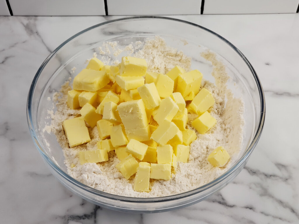 A bowl of flour topped with cubed butter.