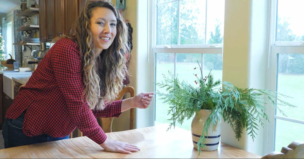 A woman standing next to a table with an evergreen Christmas centerpiece.