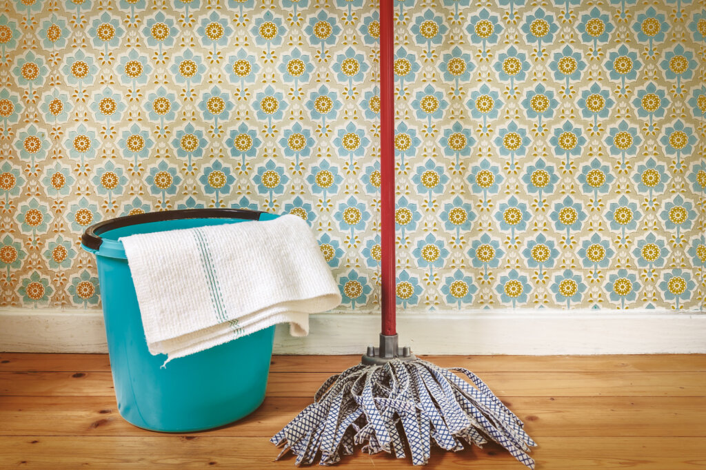 A mop and a bucket leaning against a wallpapered wall.