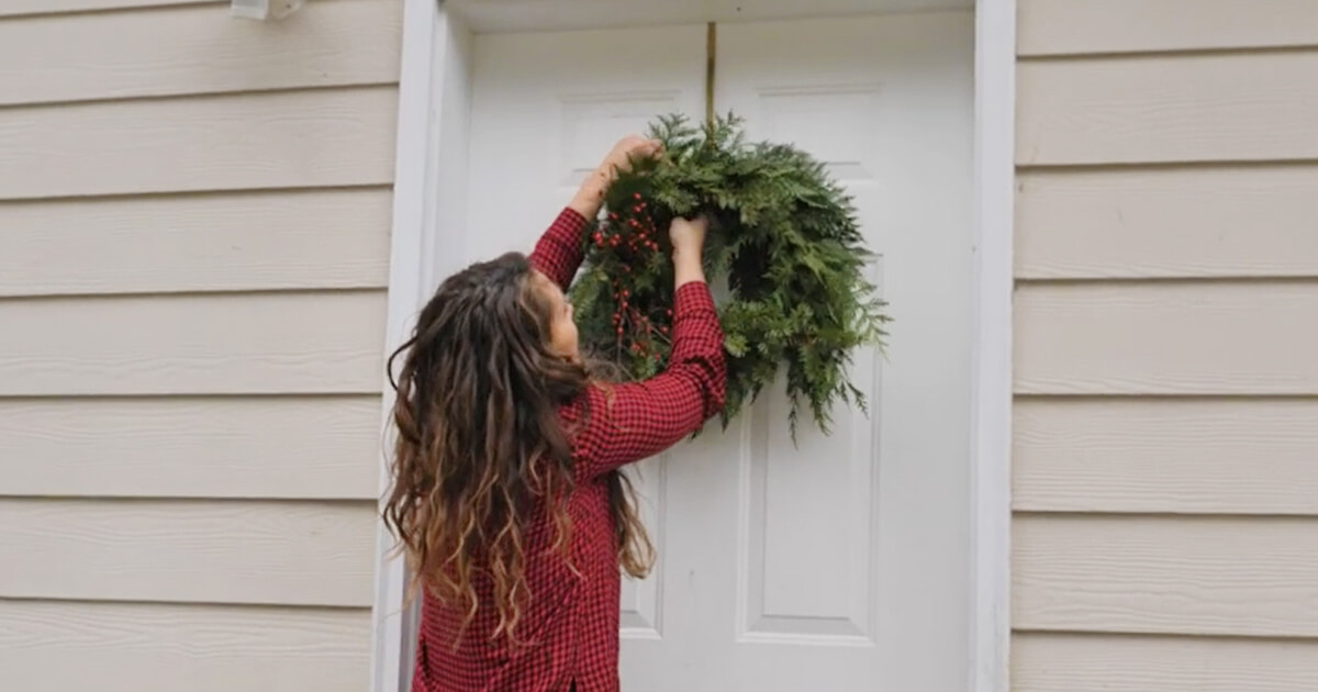A woman hanging a Christmas wreath on her front door.