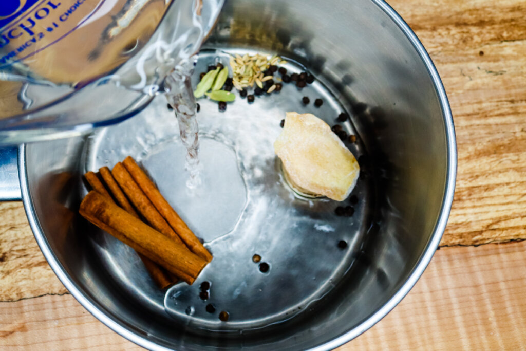 Spices for chai tea concentrate in a saute pot with water being poured in.