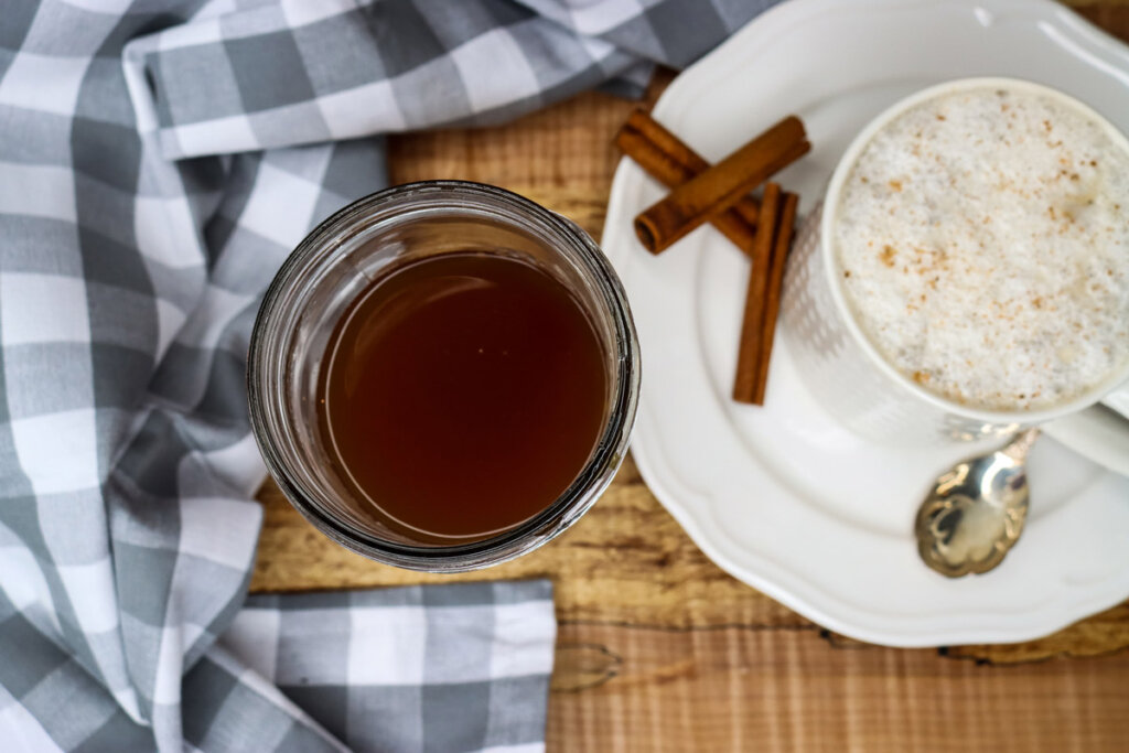 Photo of chai tea concentrate in a jar with a chai tea latte in a cup on a saucer next to it.