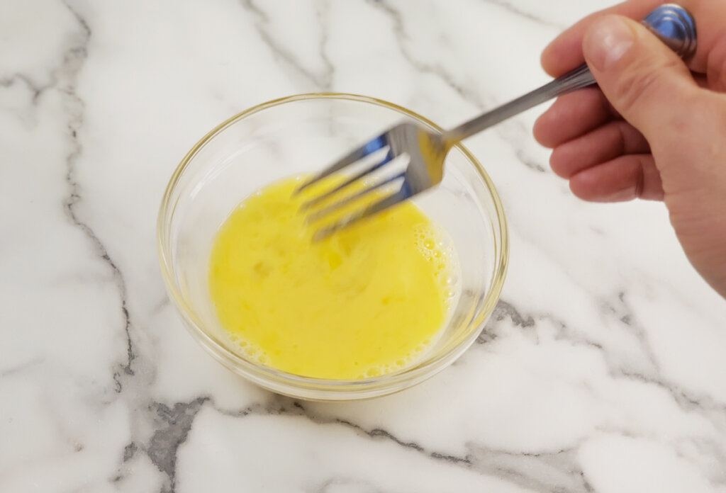 Egg and vinegar being stirred together in a bowl with a fork.