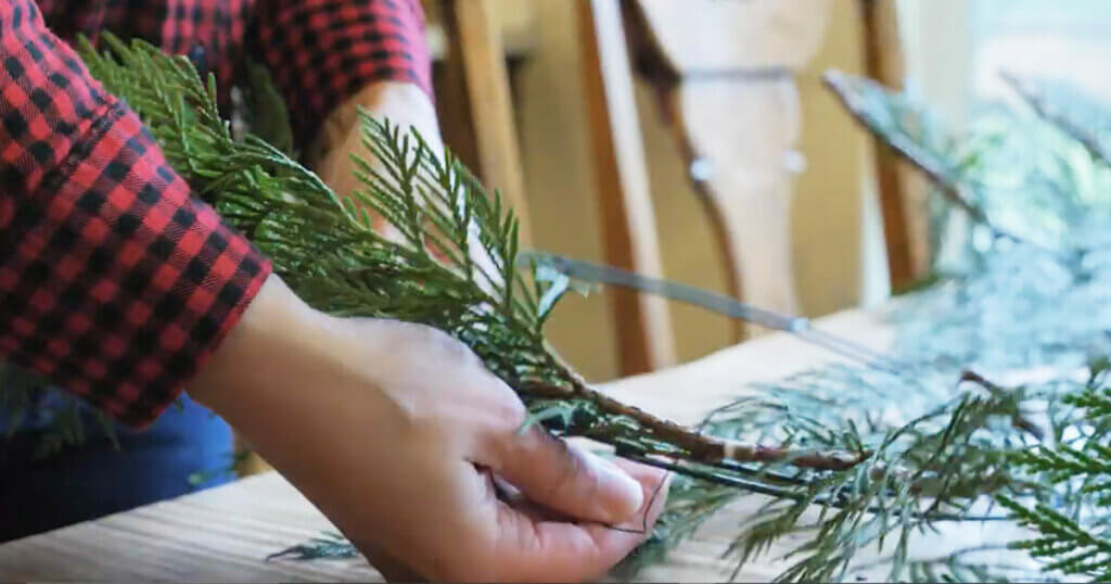 Upclose photo of hands securing a branch to a wreath form.