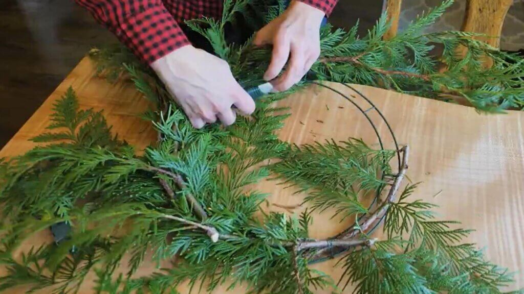 Hands securing evergreen boughs to a wreath form.