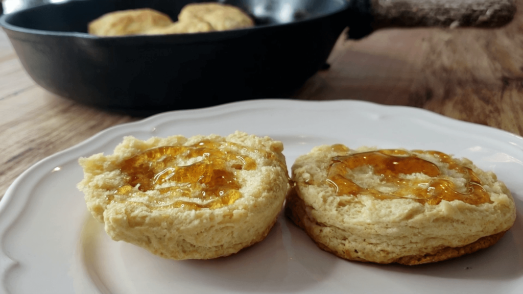 A biscuit in half on a white plate, drizzled with honey.