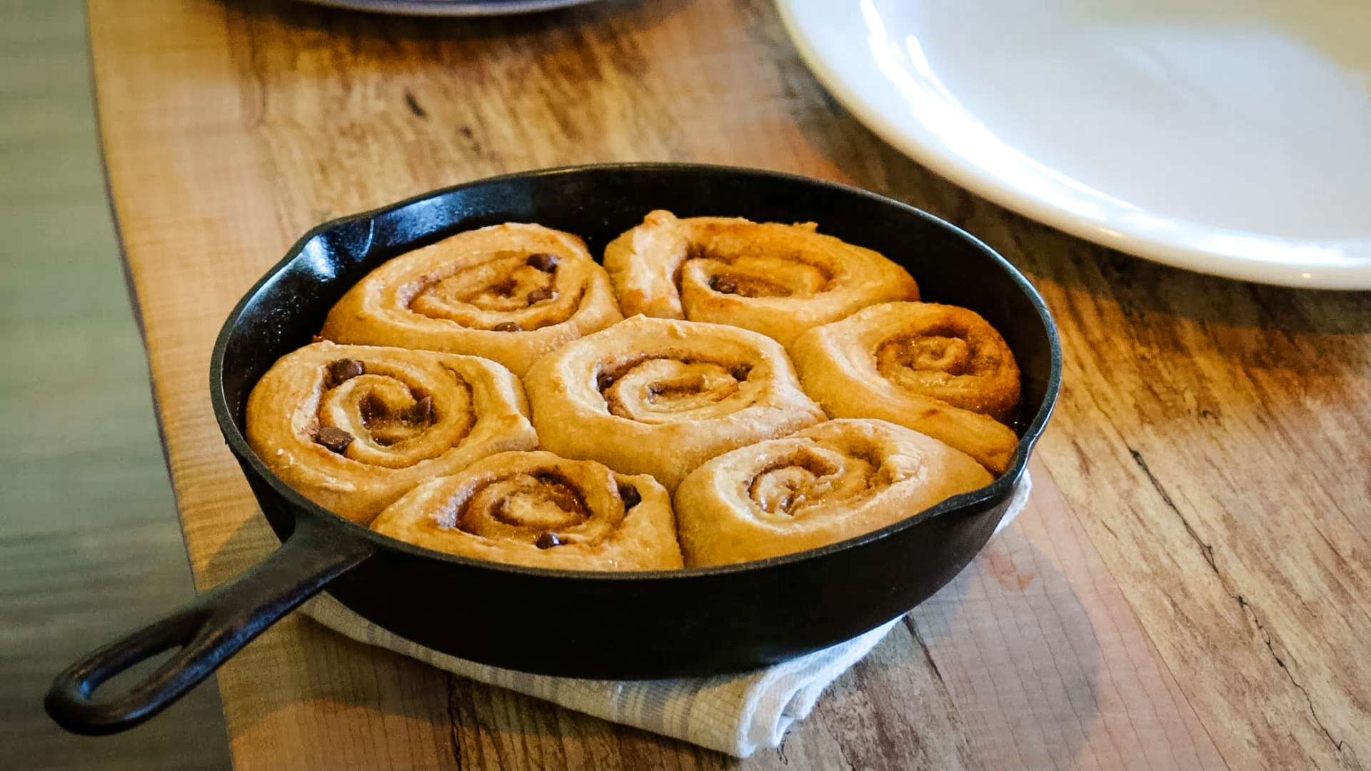 Chocolate caramel cinnamon rolls baked in a cast iron pan sitting on a table.