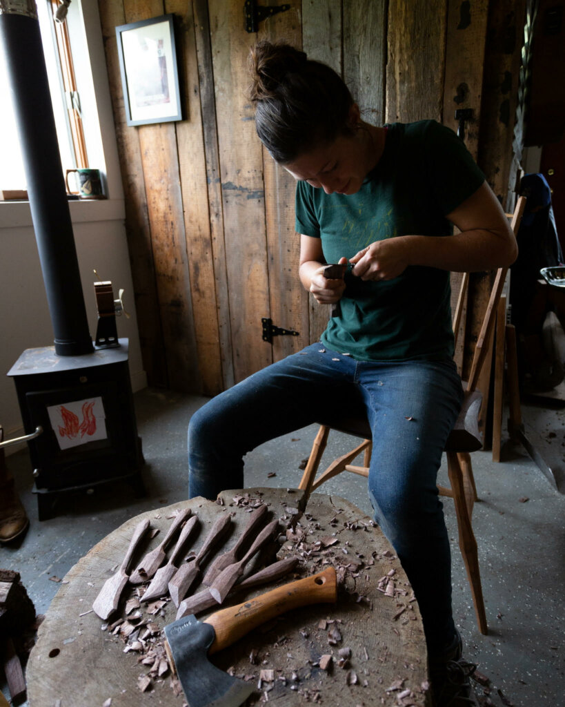 A woman sitting on a chair woodworking in a shop.