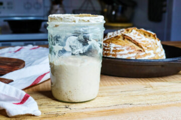 Sourdough starter in a jar with a loaf of bread in the background.