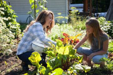 A woman and daughter picking vegetables in the garden.