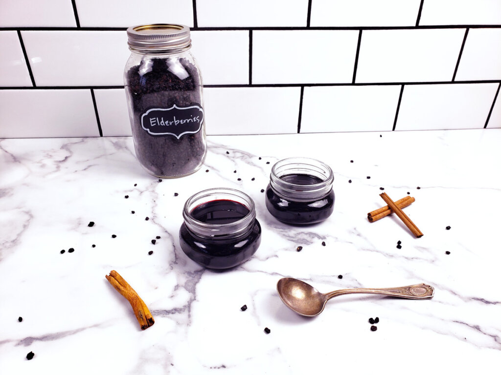 Dried elderberries in a jar and two small jars of elderberry syrup sitting on a counter.